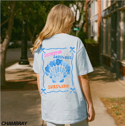 Person wearing a light blue t-shirt with a graphic design on the back, standing outdoors.