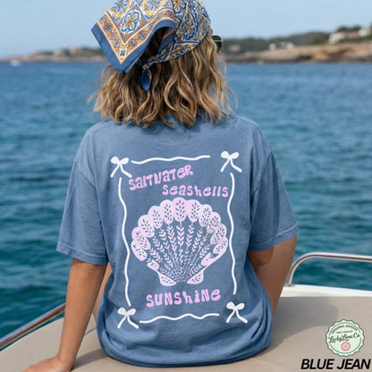 Person wearing a blue t-shirt with a shell design and text by the water