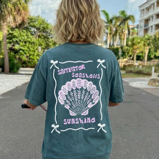 Person wearing a blue t-shirt with a shell design and text in an outdoor setting.