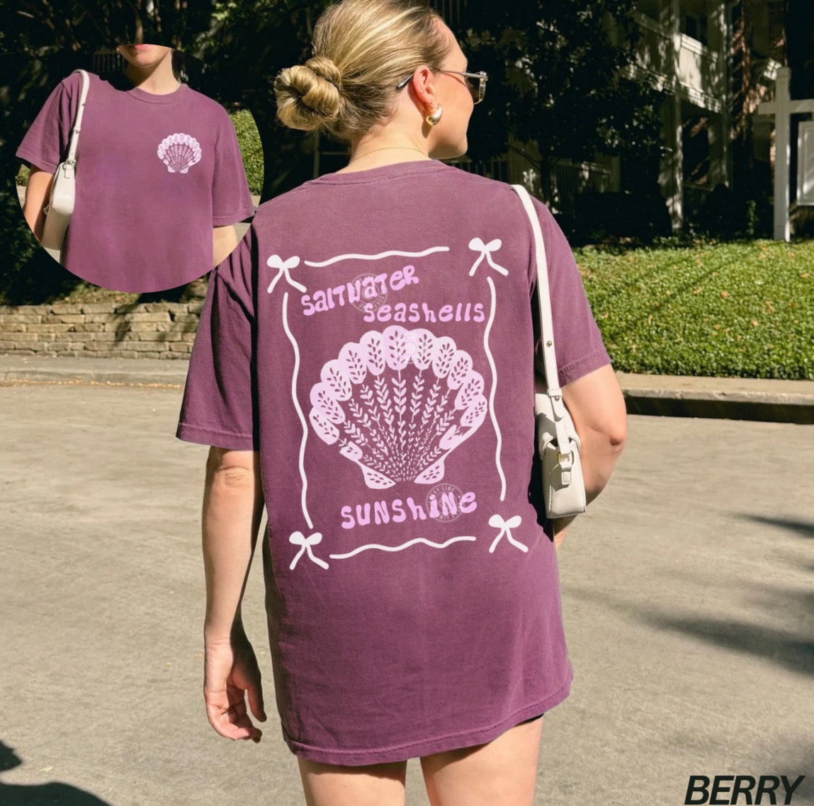 Person wearing a purple t-shirt with a shell design and text outdoors.