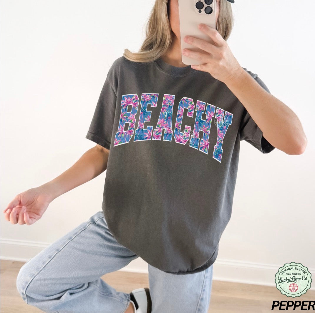 Person wearing a gray t-shirt with 'BEACHY' printed in colorful letters, taking a mirror selfie.