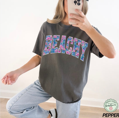 Person wearing a gray t-shirt with 'BEACHY' printed in colorful letters, taking a mirror selfie.
