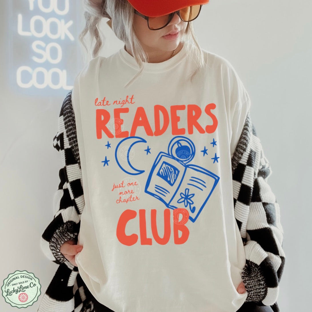 Person wearing an ivory shirt with 'Late Night Readers Club' design, holding a black and white patterned bag.