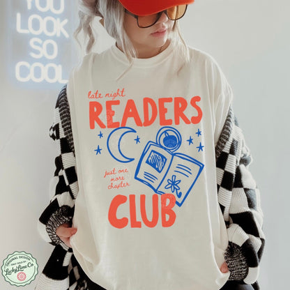 Person wearing an ivory shirt with 'Late Night Readers Club' design, holding a black and white patterned bag.