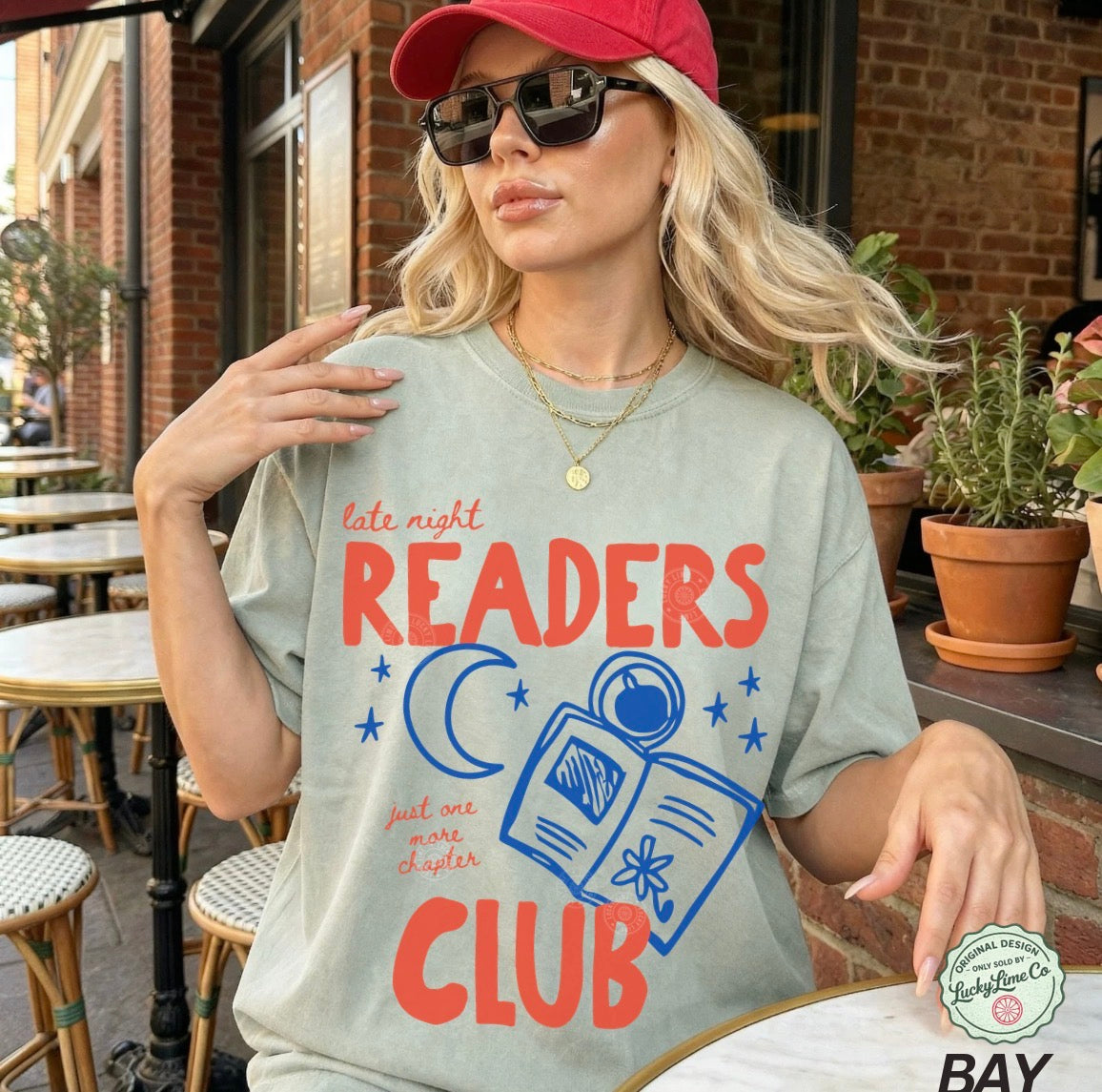 Woman wearing a t-shirt with 'Late Night Readers Club' design outdoors.
