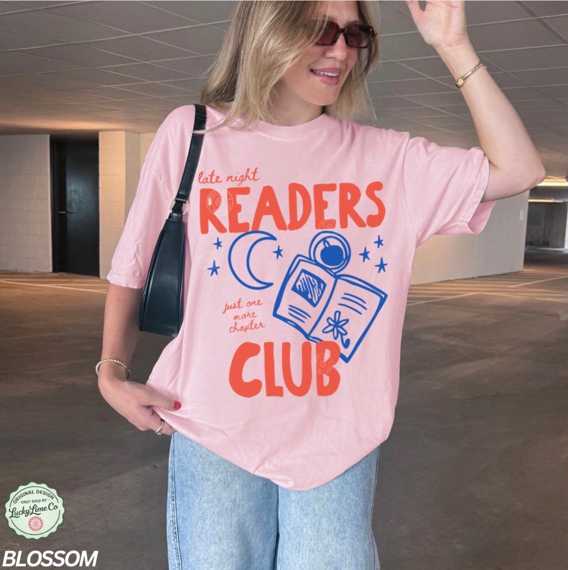 Person wearing a pink t-shirt with 'Late Night Readers Club' design in an indoor setting.