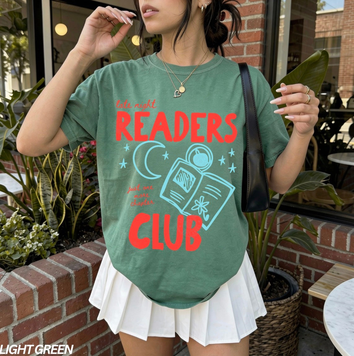 Person wearing a green t-shirt with 'Readers Club' text and graphics outdoors.