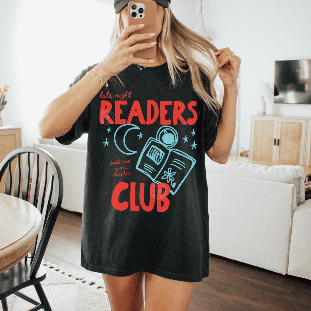 Person wearing a black t-shirt with 'late night readers club' design in a living room.