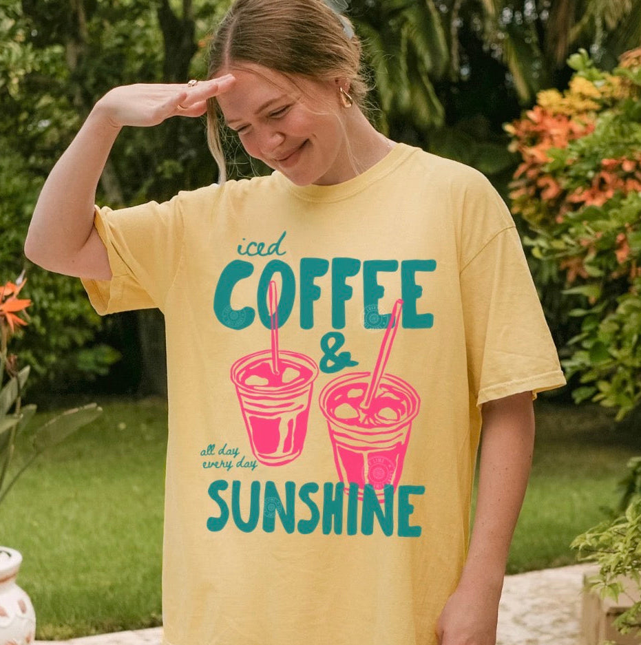 Woman wearing a yellow t-shirt with 'iced coffee & sunshine' design outdoors.