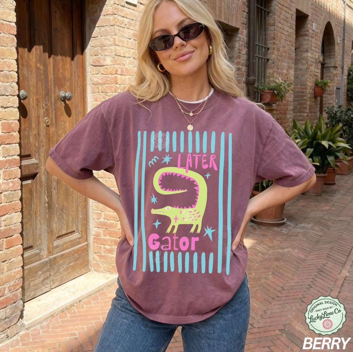 Woman wearing a purple t-shirt with a alligator graphic and text, standing in front of a brick building.