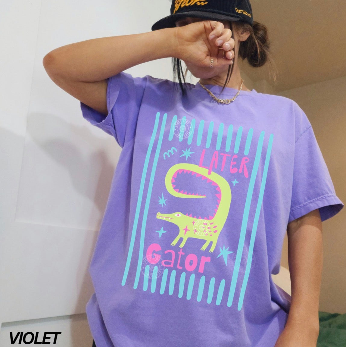 Person wearing a purple t-shirt with a colorful 'Later Gator' design, standing against a plain background.