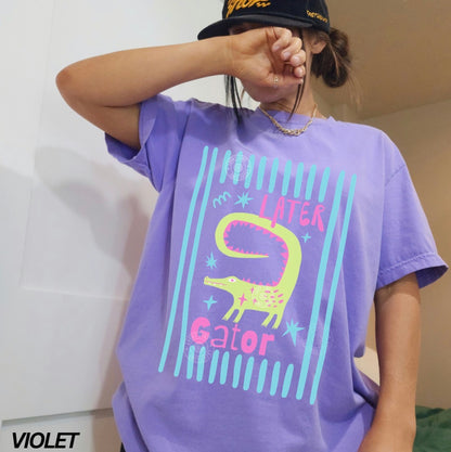 Person wearing a purple t-shirt with a colorful 'Later Gator' design, standing against a plain background.