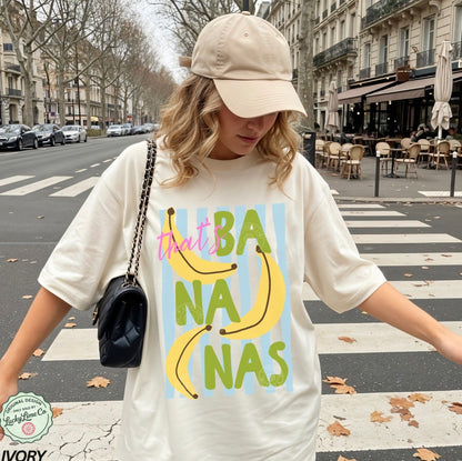 Girl wearing an ivory shirt that says “that’s bananas” standing on a street