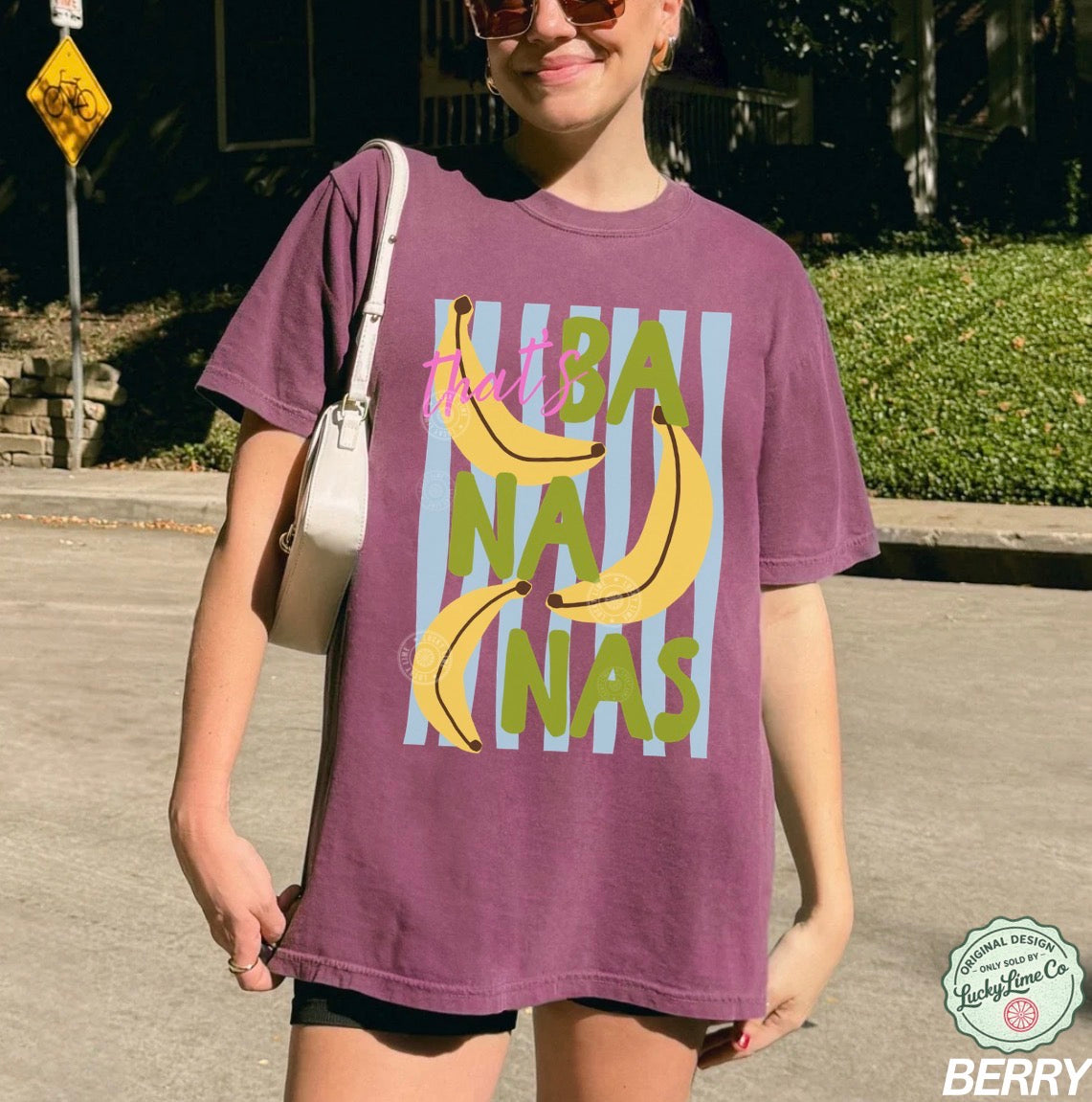 Person wearing a purple t-shirt with banana graphic and text outdoors