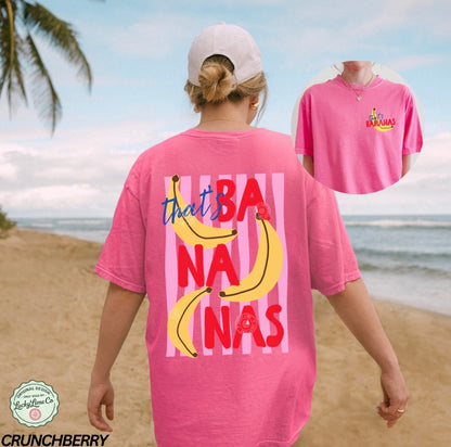 Person wearing a pink t-shirt with banana graphics and text on a beach.