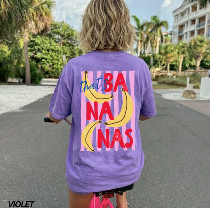 Person wearing a purple t-shirt with colorful text and banana graphics outdoors.
