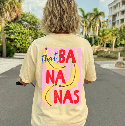 Person wearing a yellow t-shirt with 'that's bananas' design, riding a bike outdoors.