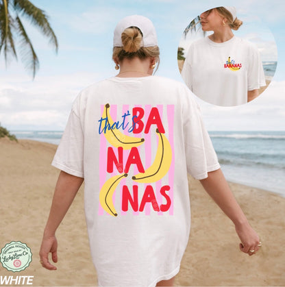 Person wearing a white t-shirt with colorful text and banana graphics on a beach.