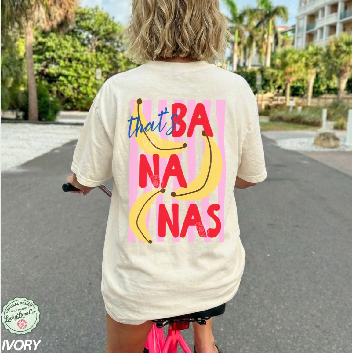 Person wearing an ivory  t-shirt with 'that's bananas' design, riding a scooter outdoors.