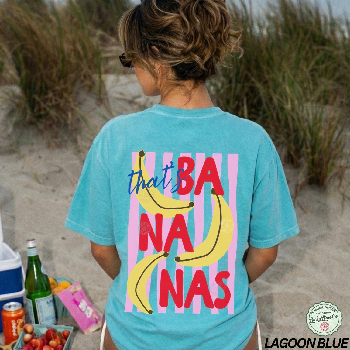 Person wearing a turquoise t-shirt with colorful text and banana graphics on a beach.
