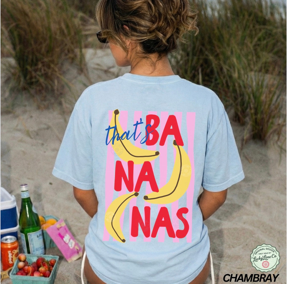 Person wearing a light blue t-shirt with colorful 'bananas' design on a beach.