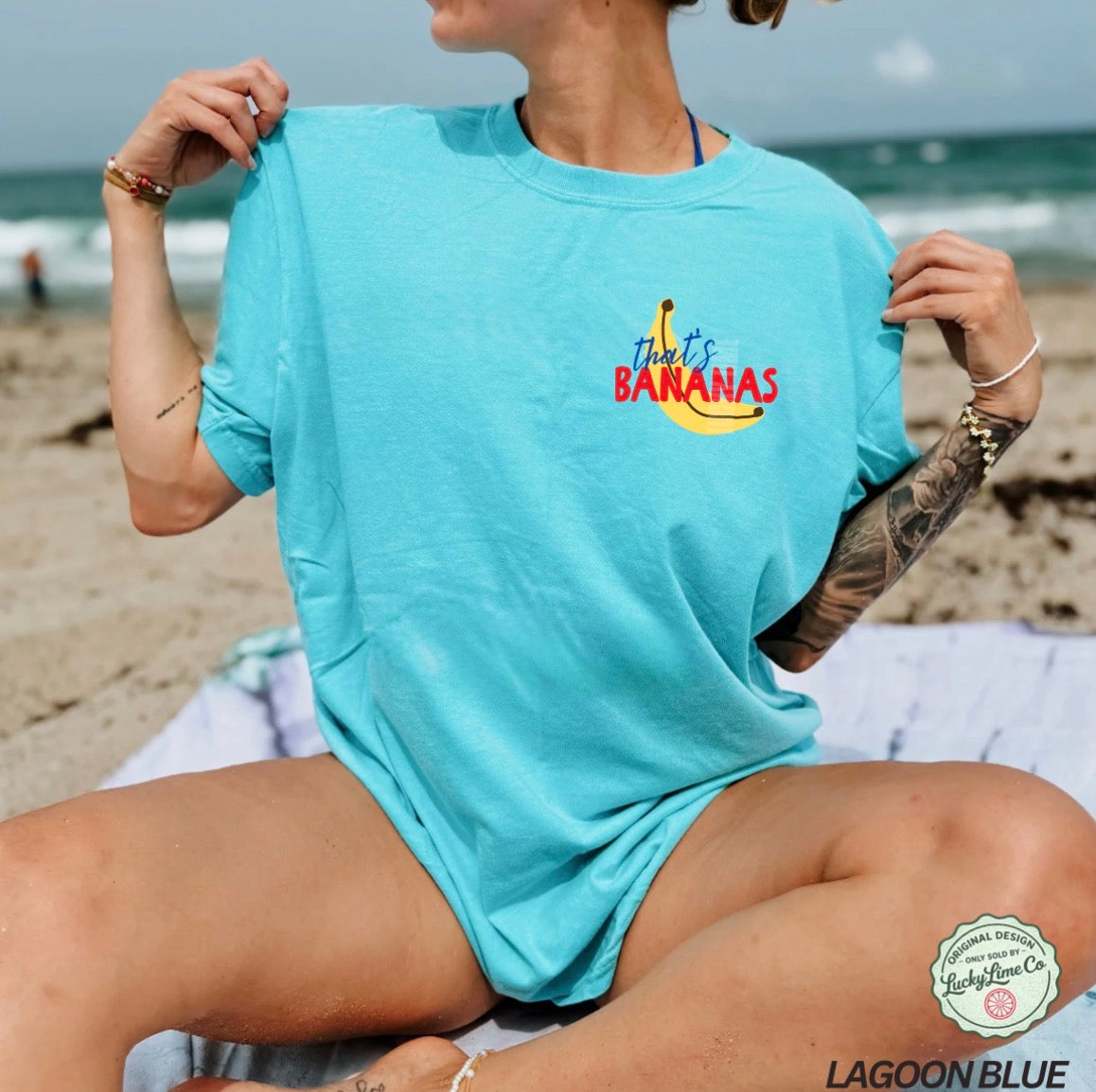 Person wearing a light blue t-shirt with 'That's Bananas' text on a beach.
