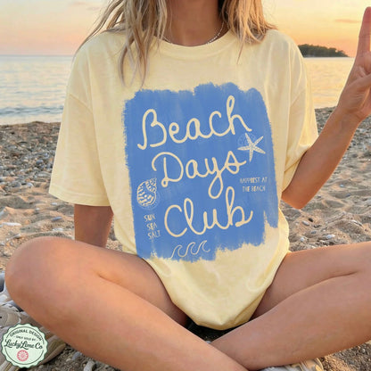 Person wearing a 'Beach Days Club' t-shirt on a beach
