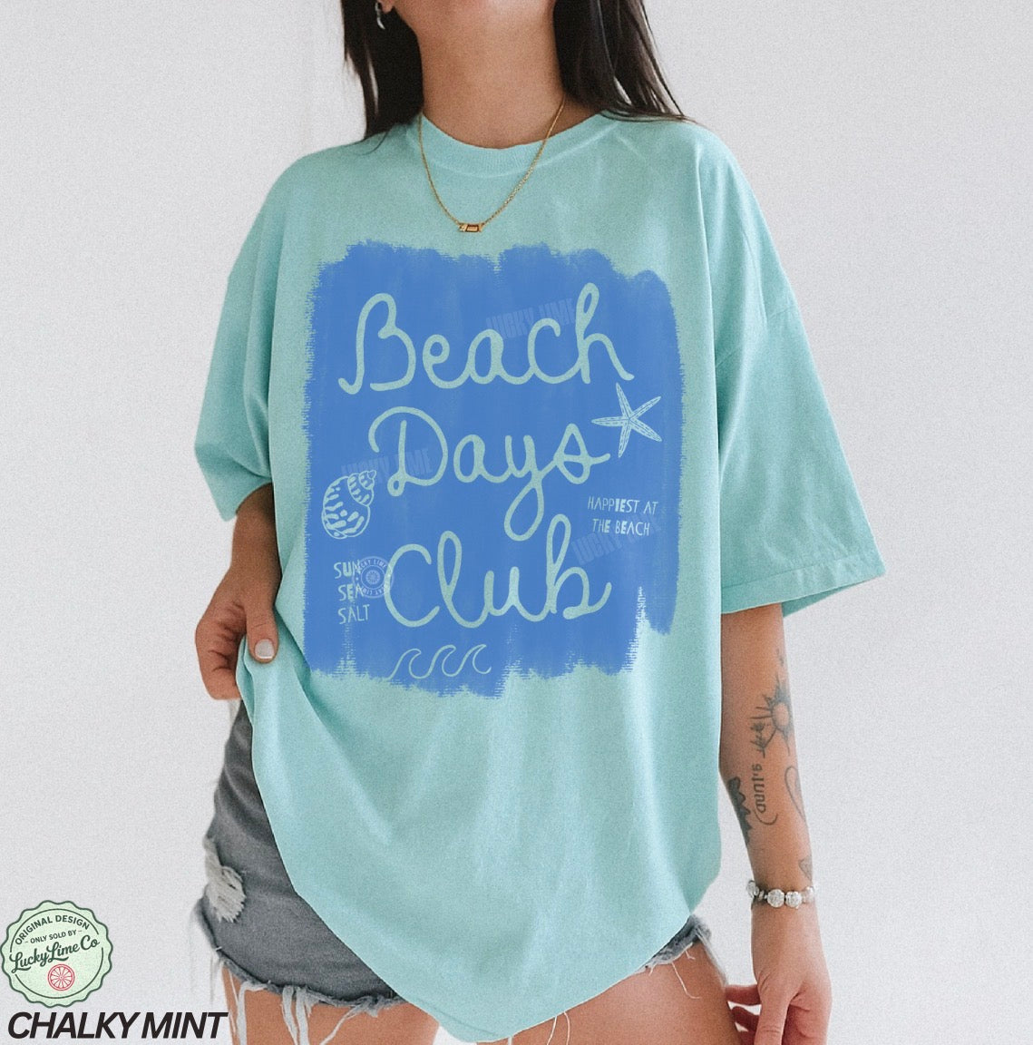 Person wearing a light blue t-shirt with 'Beach Days Club' design on a plain background