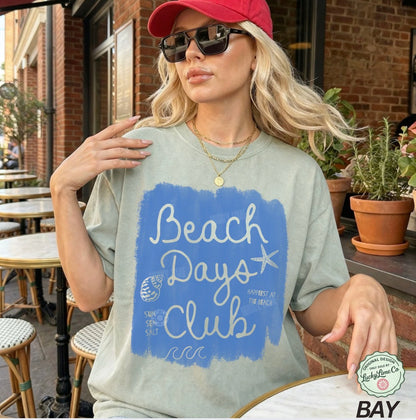 Woman wearing a 'Beach Days Club' t-shirt in an outdoor setting.