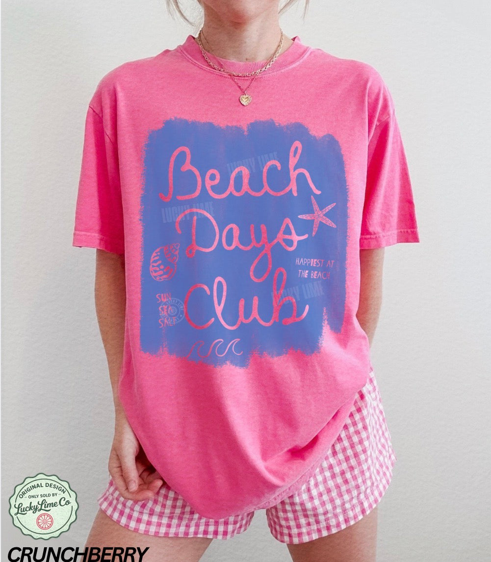 Person wearing a pink 'Beach Days Club' t-shirt with a blue graphic on a plain background