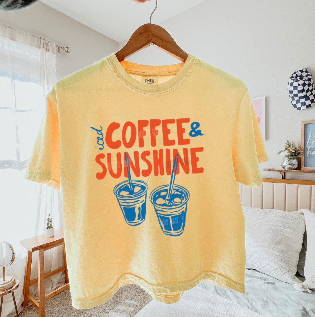 Yellow t-shirt with 'Coffee & Sunshine' text and graphics on a hanger in a bedroom.