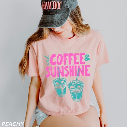 Person wearing a pink t-shirt with 'Coffee & Sunshine' text and graphics, paired with a cap.