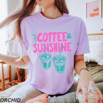 Person wearing a purple t-shirt with 'Coffee & Sunshine' text and graphics, sitting indoors.