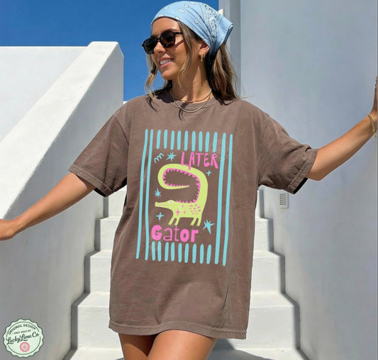 Woman wearing a brown t-shirt with a alligator graphic and text, standing on white steps.