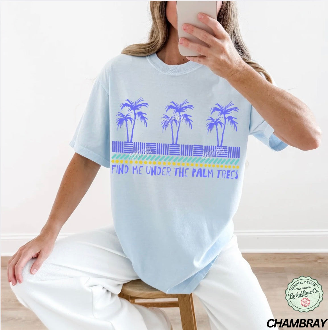 Person wearing a light blue t-shirt with palm tree design and text, sitting on a chair.