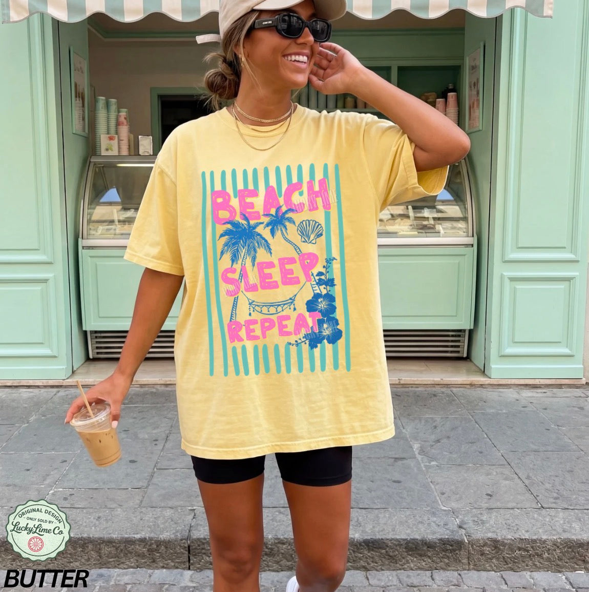 Woman wearing a yellow t-shirt with 'Beach Sleep Repeat' text and graphics, standing in front of a green building.