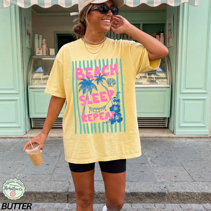 Woman wearing a yellow t-shirt with 'Beach Sleep Repeat' text and graphics, standing in front of a green building.