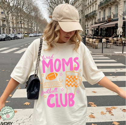 Person wearing a t-shirt with 'tired moms football club' text on a city street.