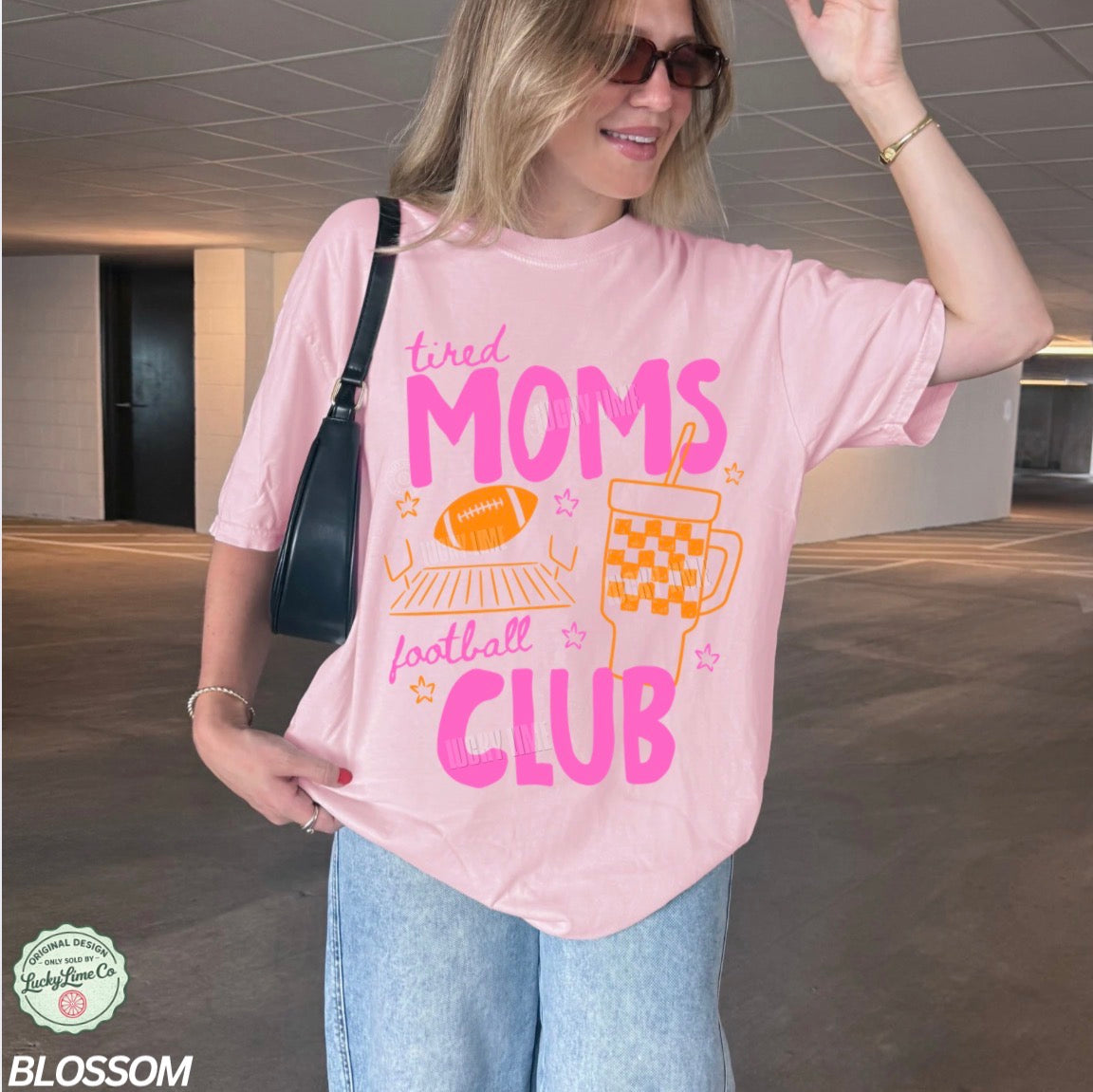 Woman wearing a pink t-shirt with 'tired moms football club' text in an indoor setting.