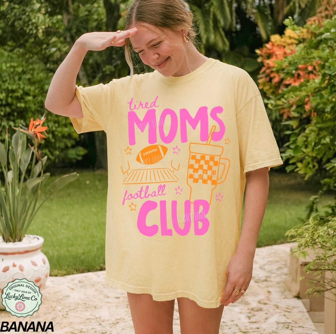 Person wearing a yellow t-shirt with 'tired moms football club' text and graphics outdoors.