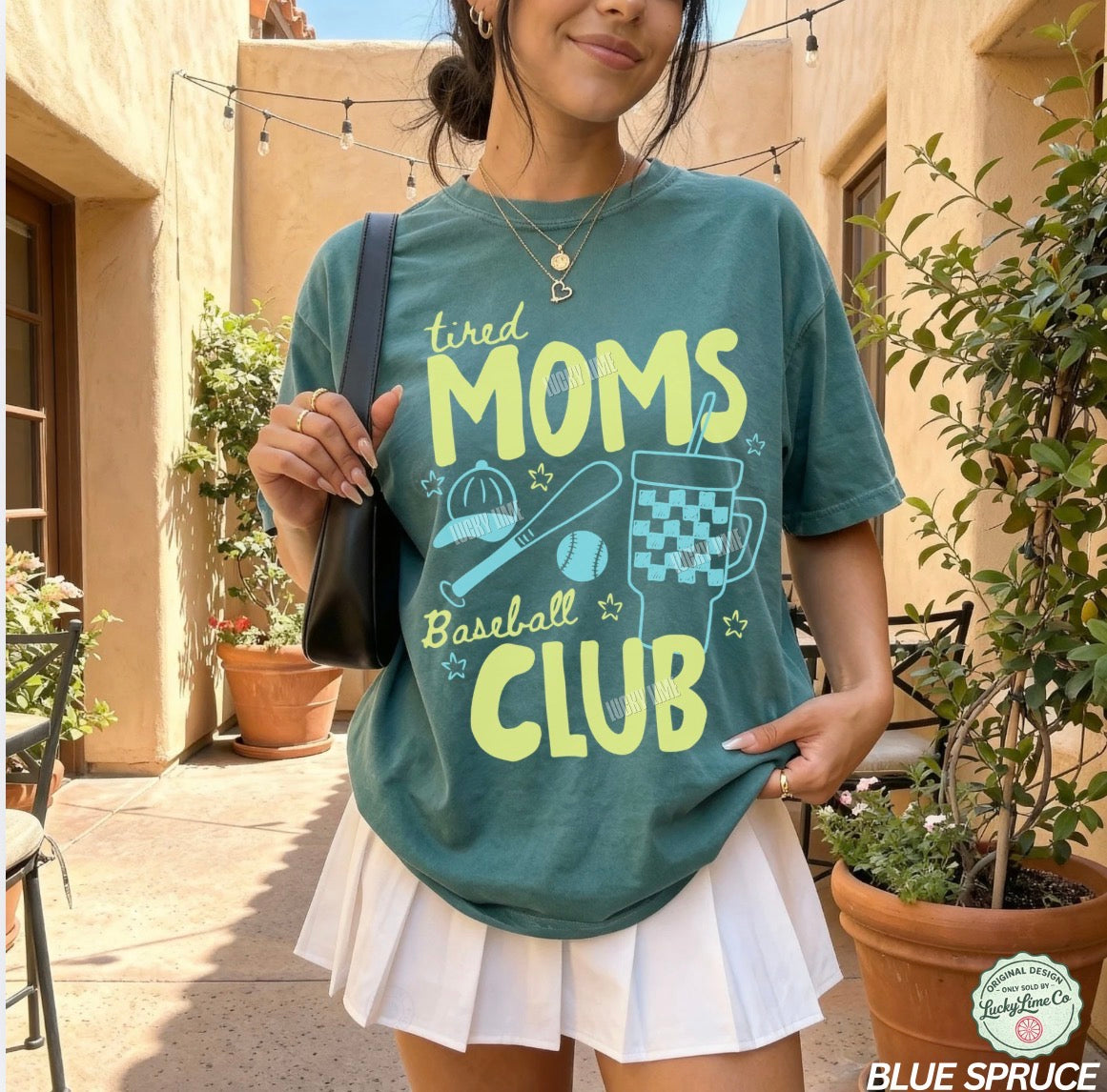 Person wearing a teal t-shirt with 'tired moms baseball club' text in an outdoor setting.