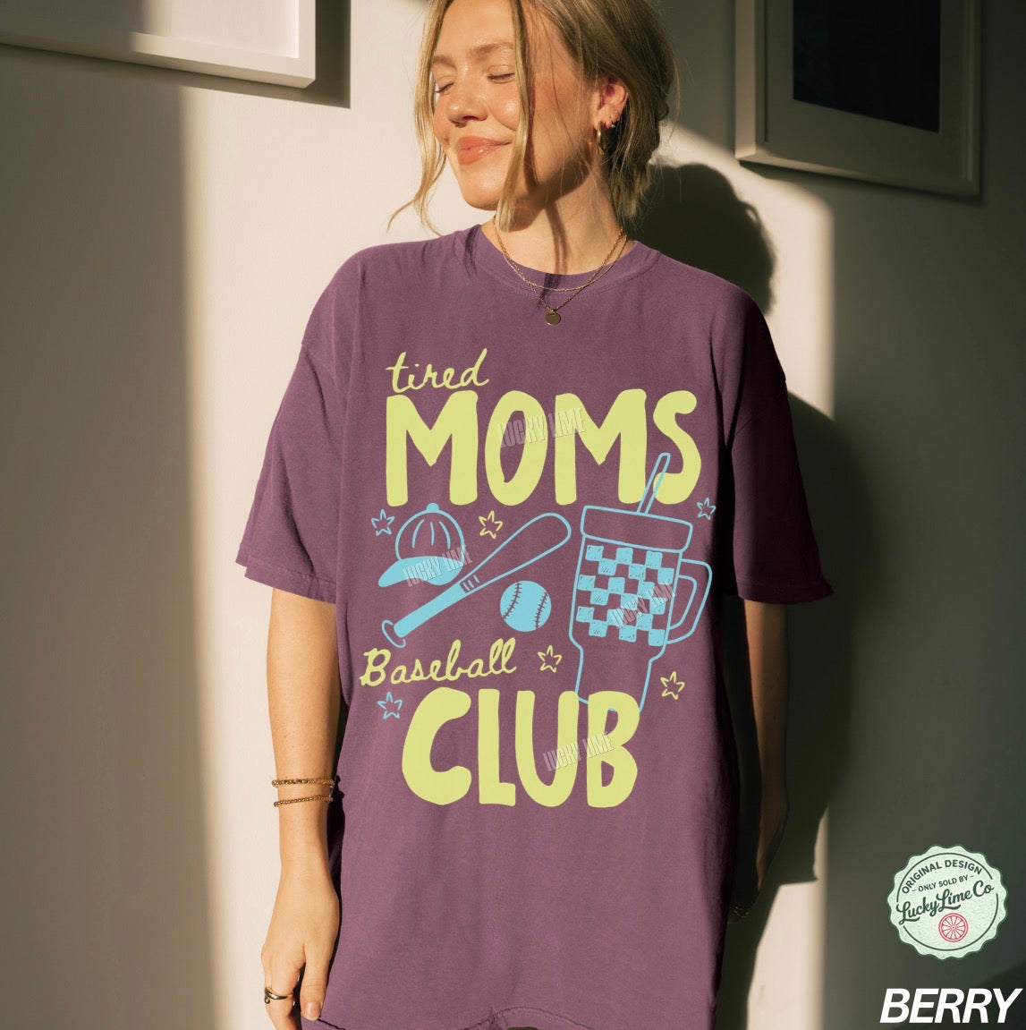 Person wearing a purple t-shirt with 'tired moms baseball club' text and graphics.