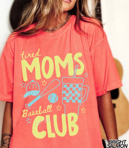 Person wearing a coral t-shirt with 'tired moms baseball club' text and graphics.