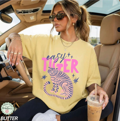 Woman in a car wearing a 'easy tiger' shirt and holding a drink.