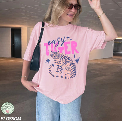 Person wearing a pink t-shirt with a tiger graphic and text, standing in an indoor setting.