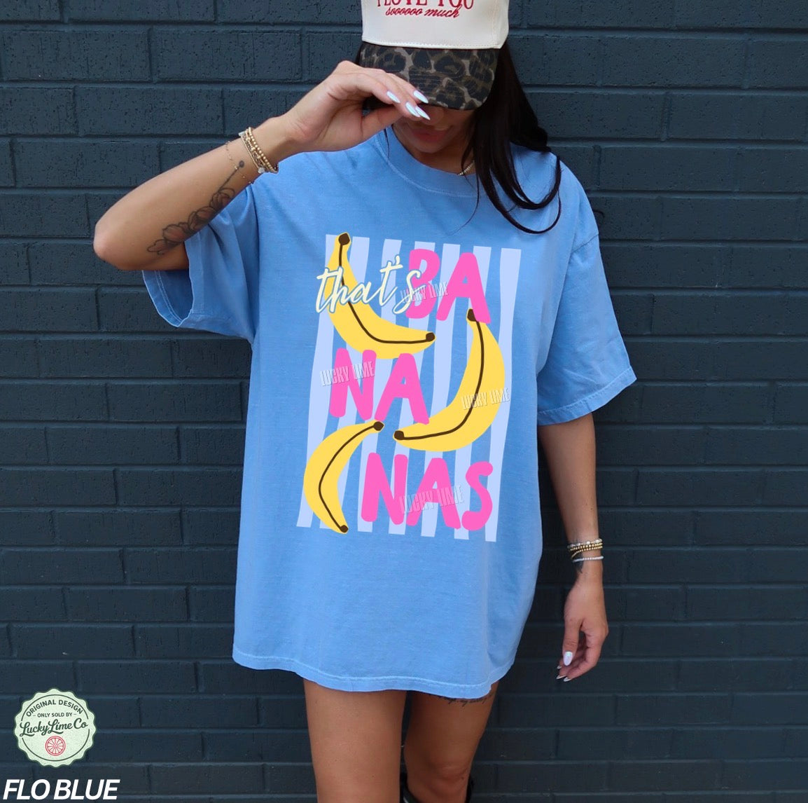 Person wearing a blue t-shirt with colorful text and banana graphics against a dark brick wall.