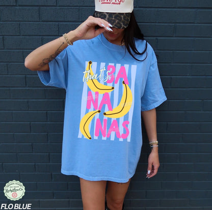 Person wearing a blue t-shirt with colorful text and banana graphics against a dark brick wall.