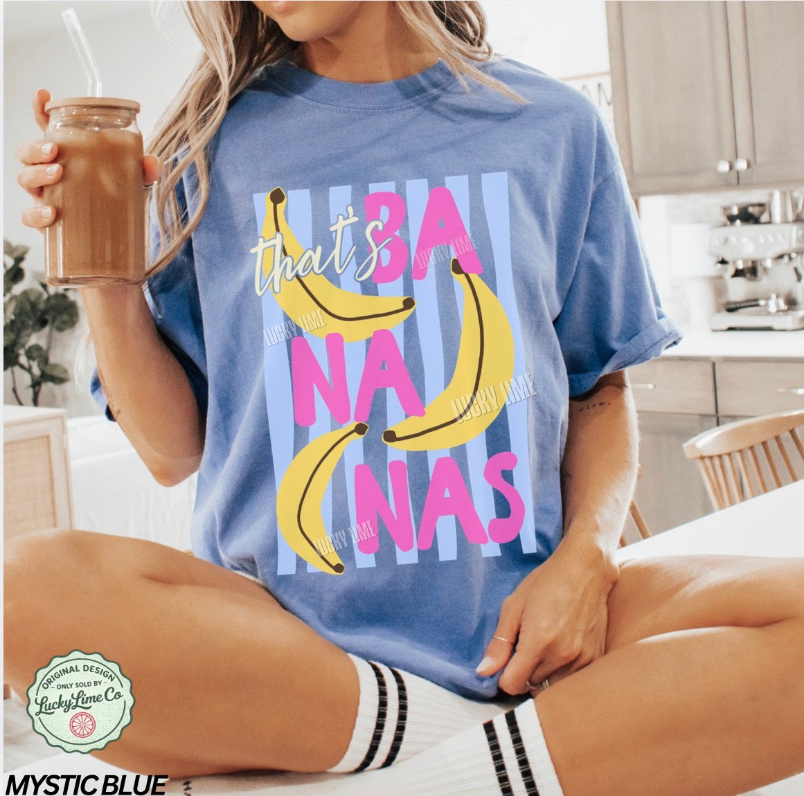 Person wearing a blue t-shirt with banana graphics and text, sitting in a kitchen.