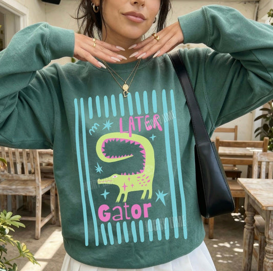 Person wearing a green sweatshirt with a a later gator graphic and text, standing outdoors.