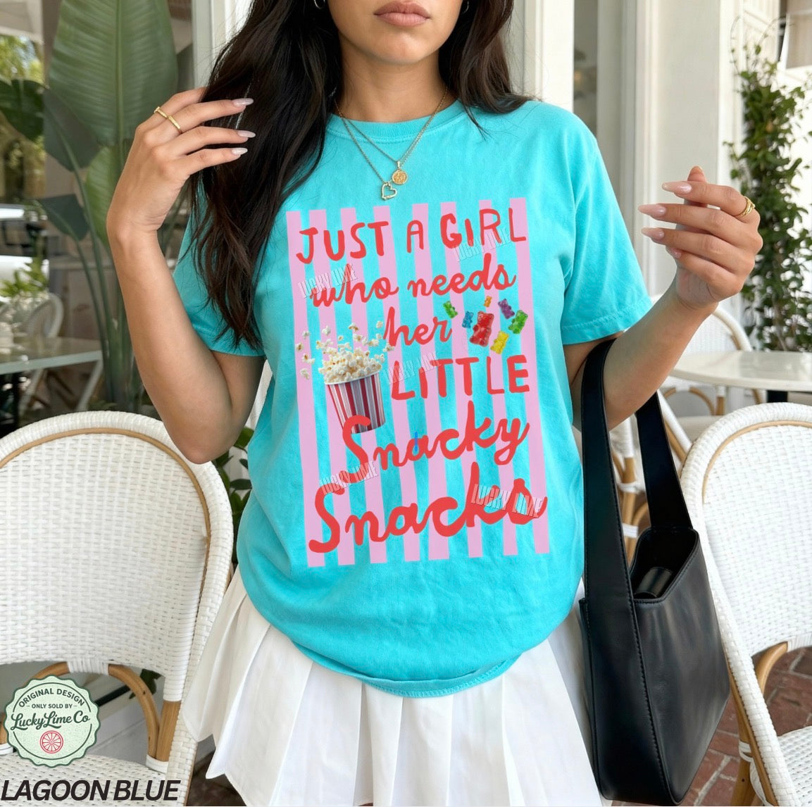 Woman wearing a turquoise t-shirt with a colorful graphic and text, standing outdoors.